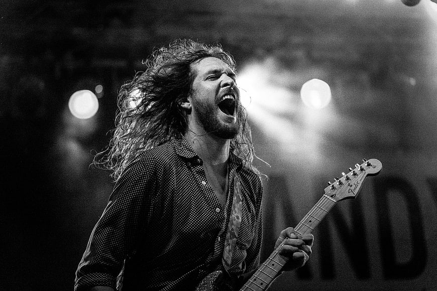 Passionate male rock musician singing and playing guitar on stage