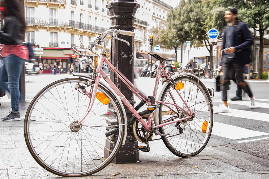 Pink bicycle locked to post on busy Paris street
