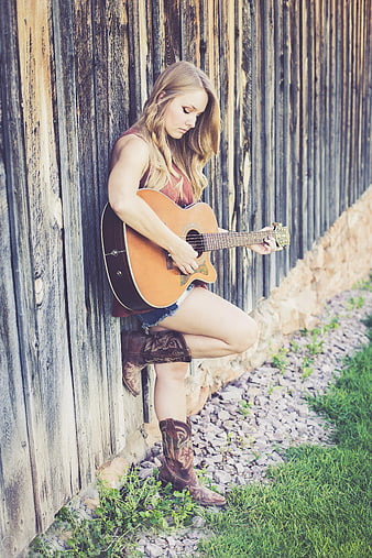 Woman playing acoustic guitar leaning against rustic wooden fence