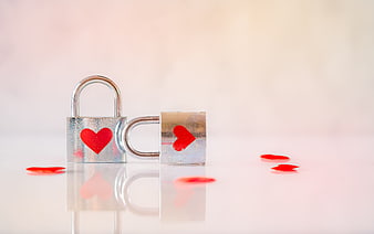 Two silver padlocks with red hearts on a reflective white surface