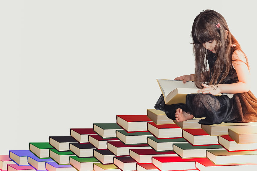 Young girl reading book on colorful book stairs