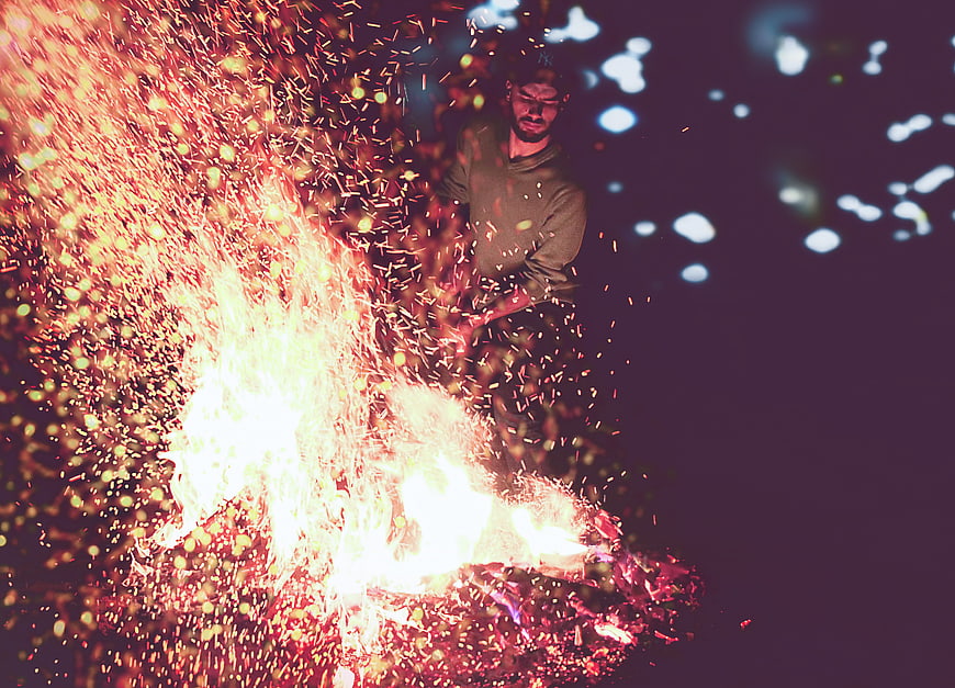 Man Tending Bonfire with Sparks Flying at Night