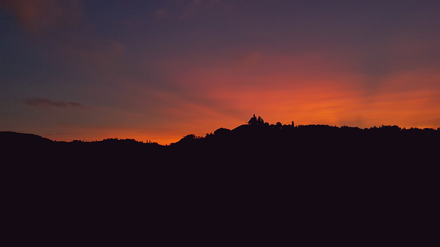 Silhouette of rolling hills against a vibrant orange and purple sunset sky