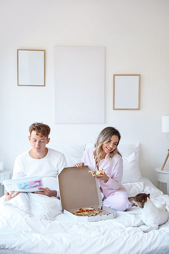 Happy couple eating pizza in bed with dog