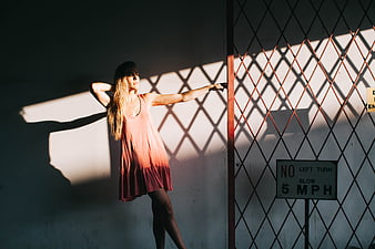 Woman in Pink Dress Leaning Against Wall with Fence Shadows