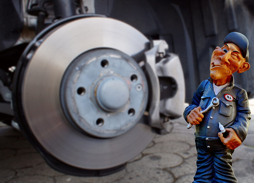 Mechanic figurine inspecting car brake disc and caliper