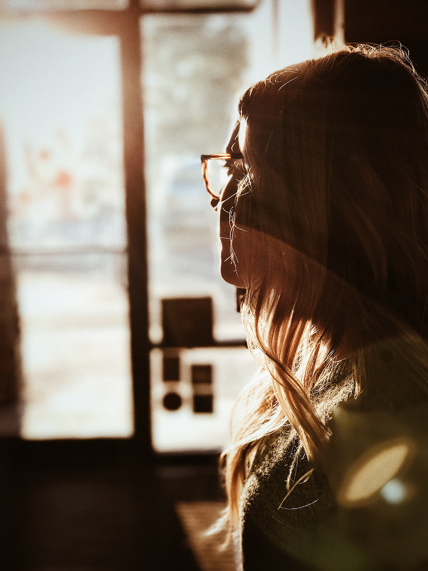 Woman with Glasses Looking Out Window in Sunlight