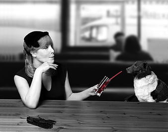Woman in vintage hat holding red cocktail glass facing dog at wooden table
