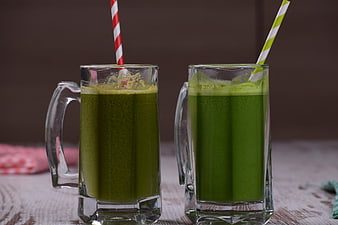 Two glasses of green vegetable juice with striped paper straws