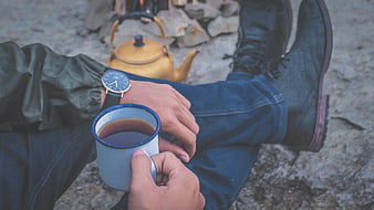 Man drinking coffee while camping with kettle and boots