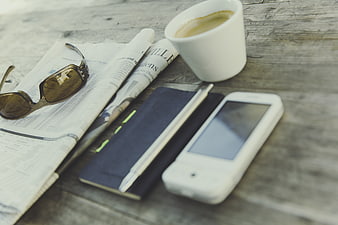 Flat lay of coffee, newspaper, sunglasses, and smartphone on rustic wood