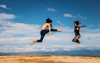 Happy couple jumping in the air on a sandy beach with mountains