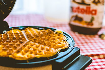 Freshly cooked waffles in waffle iron with Nutella jar