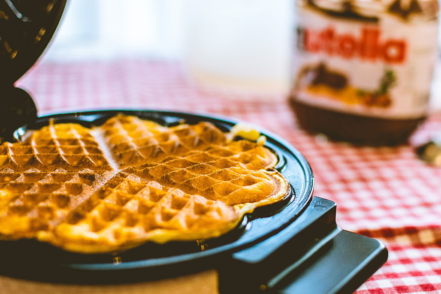 Freshly cooked waffles in waffle iron with Nutella jar
