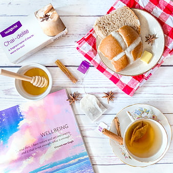Flat lay of hot cross buns, chai tea, honey, and book