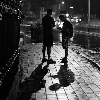 Two men looking at smartphones on wet city street at night