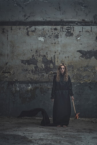 Woman in black dress holding torch against grunge wall