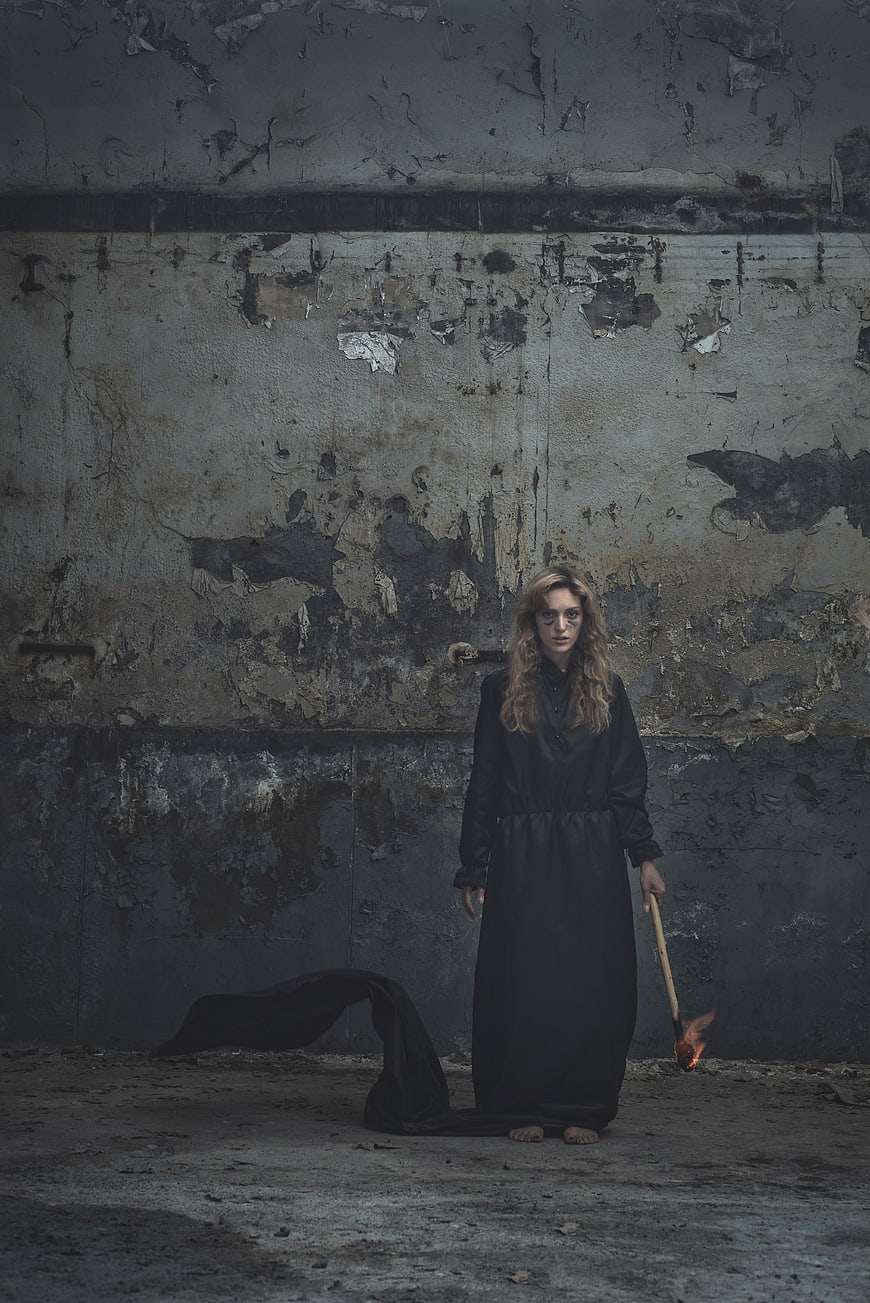 Woman in black dress holding torch against grunge wall