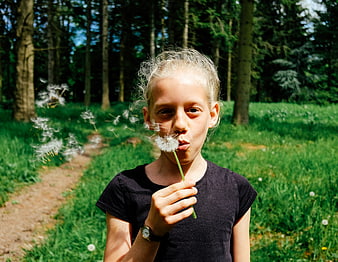 Young girl blowing dandelion seeds in a sunny forest