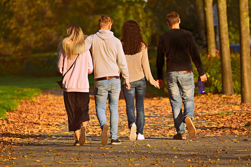 Four friends walking together on an autumn park path