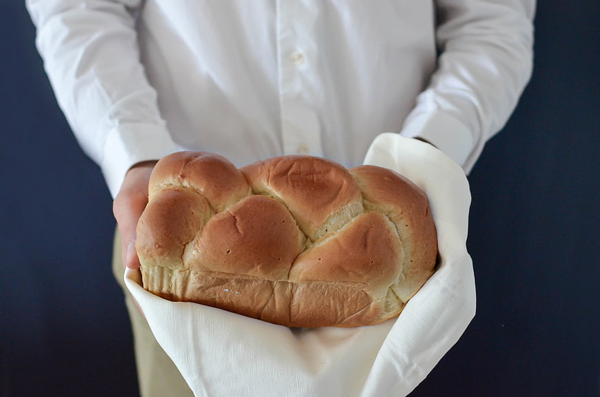 Person holding fresh loaf of bread in white cloth