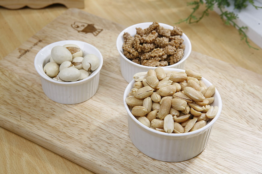 Three white bowls of peanuts, nuts, and snacks on wooden board