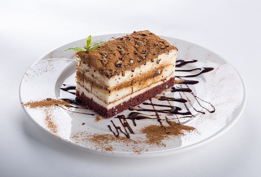 Tiramisu Cake Slice on White Plate with Chocolate Drizzle