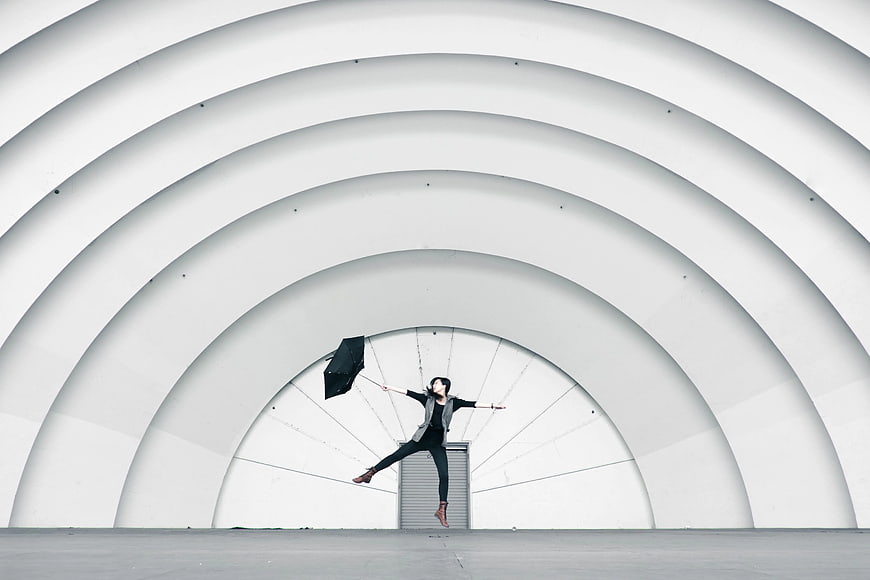 Woman Jumping with Umbrella in White Architectural Tunnel