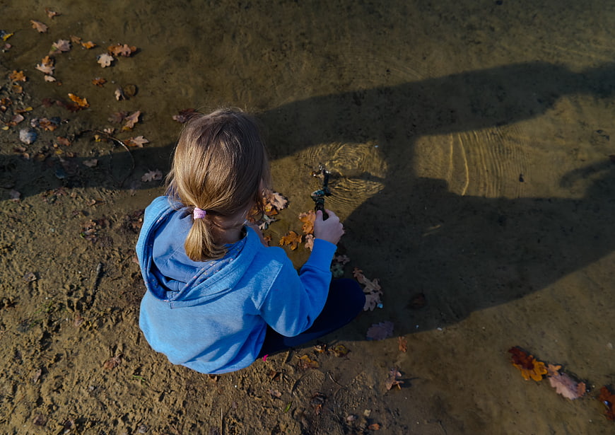 Little girl playing in shallow water with autumn leaves