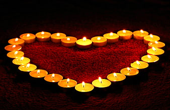Heart shape made of lit tea candles on red background