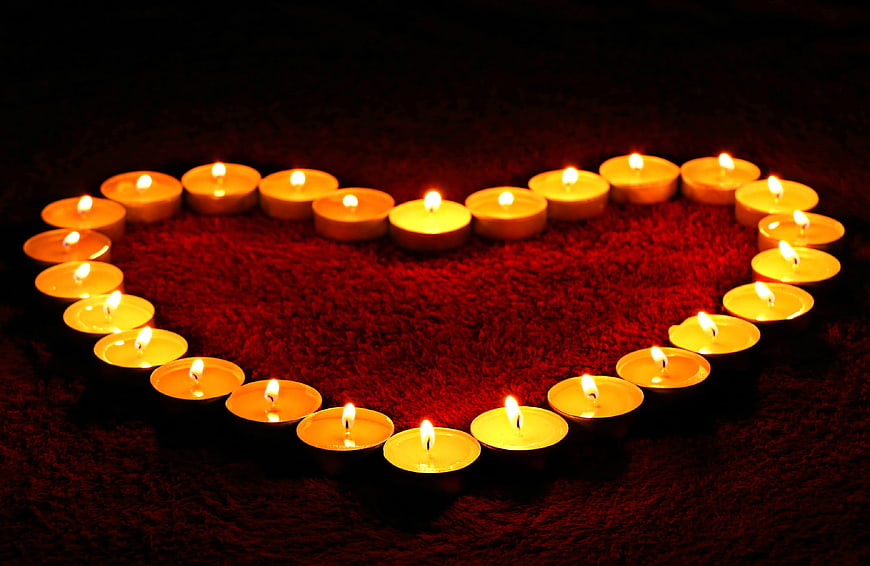 Heart shape made of lit tea candles on red background
