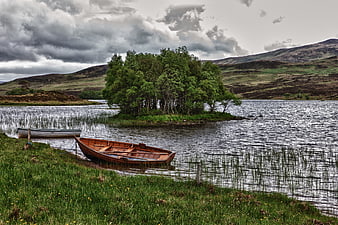 Wooden rowboat on grassy shore of Scottish loch with island