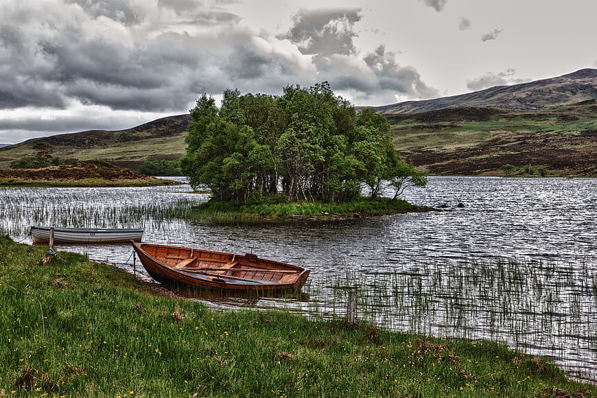 Wooden rowboat on grassy shore of Scottish loch with island