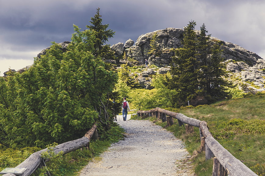 Hiker walking on mountain trail with wooden fence