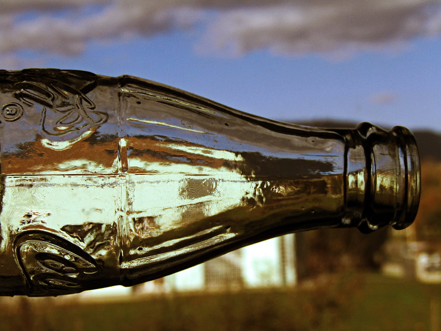 Close-up of glass bottle neck against blue sky