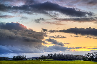 Dramatic sunset over green meadow with dark clouds