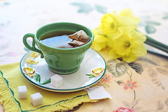 Green Tea Cup with Daffodils and Sugar Cubes on Floral Table