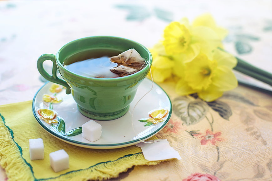 Green Tea Cup with Daffodils and Sugar Cubes on Floral Table