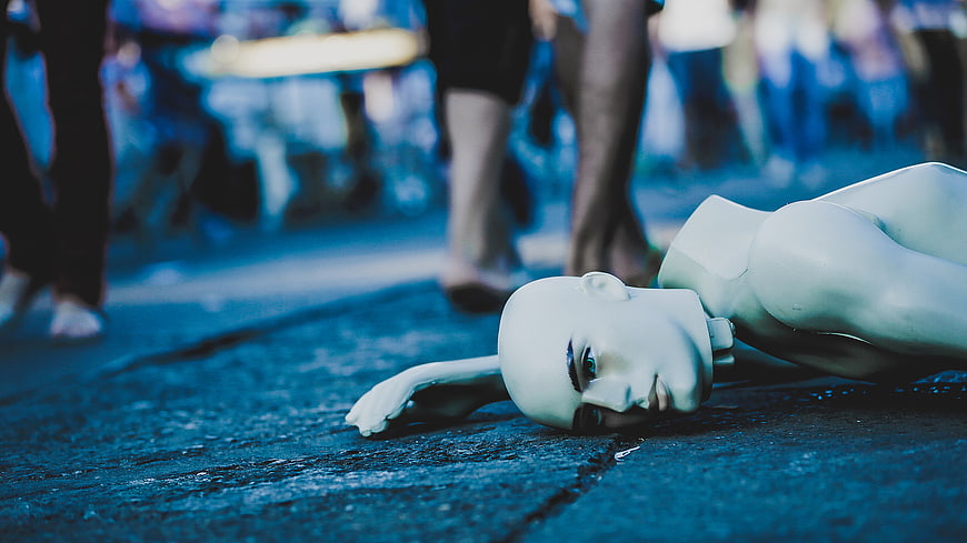 Broken white mannequin lying on blue street with blurred crowd