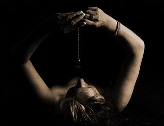Woman holding pendulum for hypnosis in dark studio