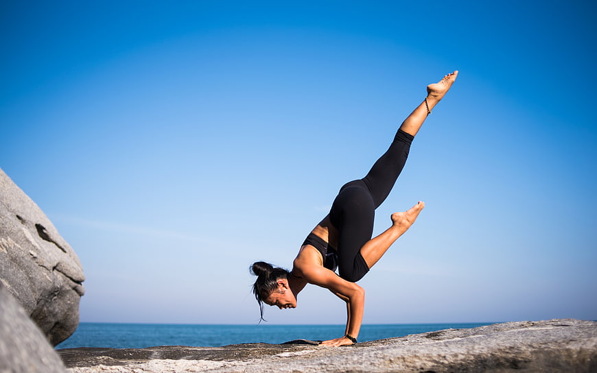 Woman performing advanced yoga pose on coastal rock