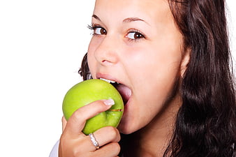 Young woman biting into a green apple on white background