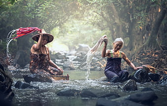 Two women washing clothes in a misty forest stream