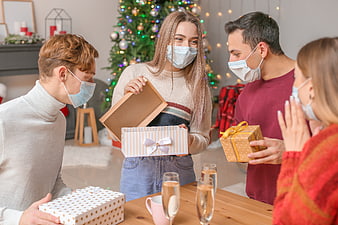 Friends exchanging Christmas gifts wearing face masks