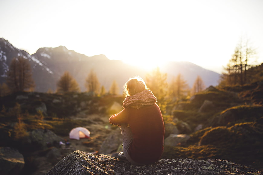 Woman sitting on rock watching mountain sunset with tent