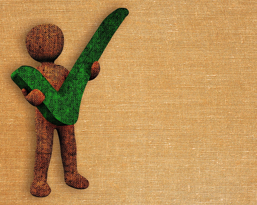 Wooden figure holding green check mark on textured background