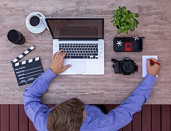 Top view of filmmaker working at wooden desk with laptop and camera