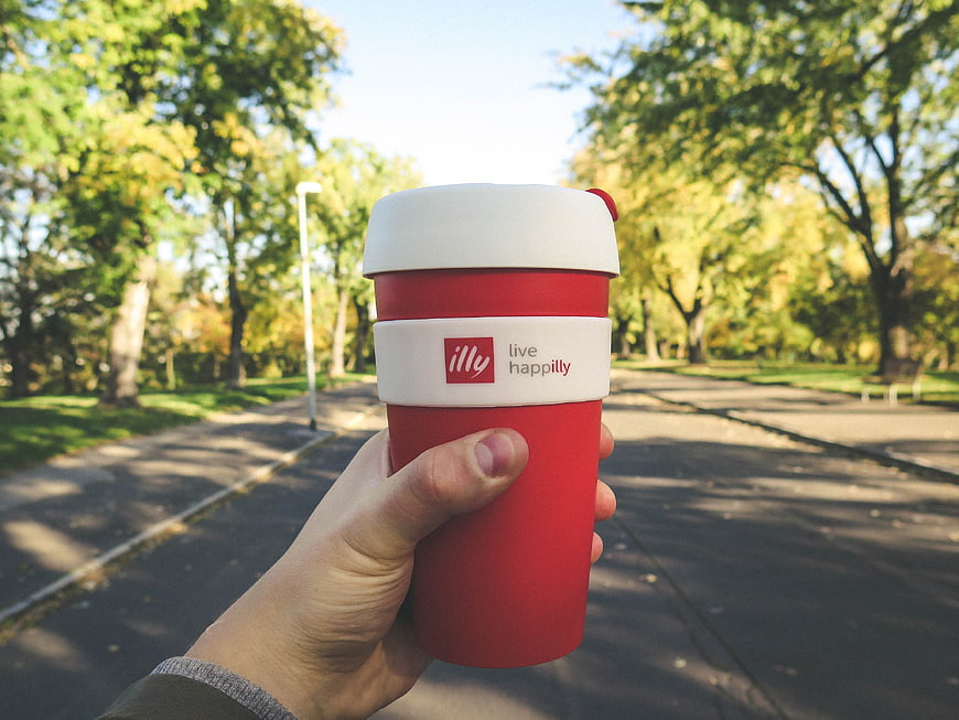 Hand holding red illy coffee cup in park