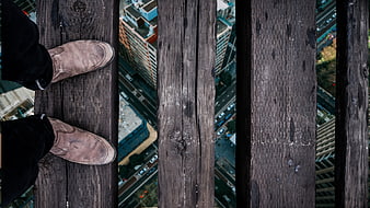 First-person view of feet on wooden planks high above city