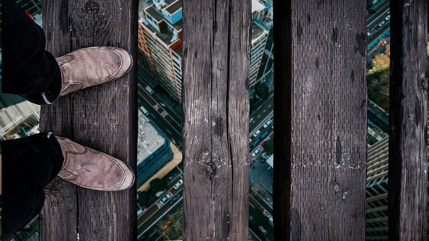First-person view of feet on wooden planks high above city